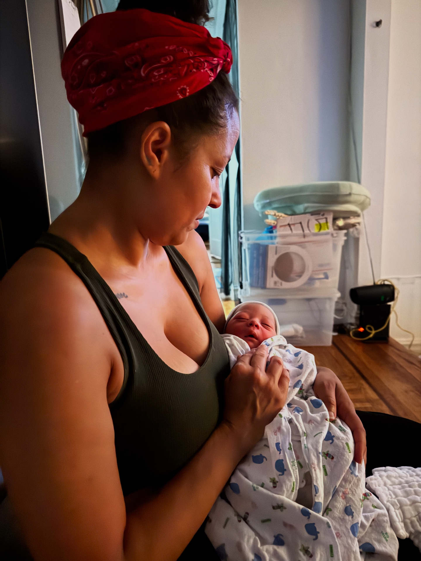 Hazel Alvarez wearing a red bandana, lovingly cradling a swaddled newborn